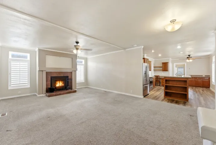 Unfurnished living room with a ceiling fan, crown molding, a fireplace, and light carpet