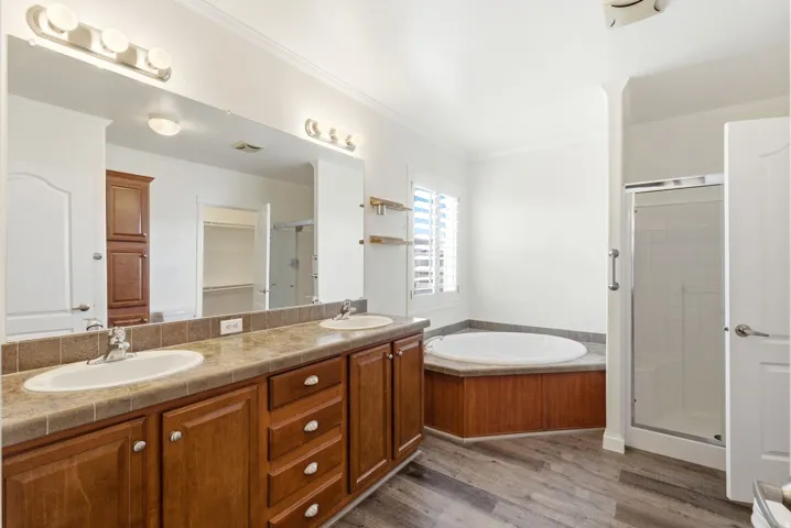 Bathroom with crown molding, double vanity, a shower stall, light wood-type flooring, and a garden tub