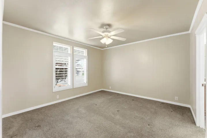 Carpeted empty room featuring ornamental molding and ceiling fan