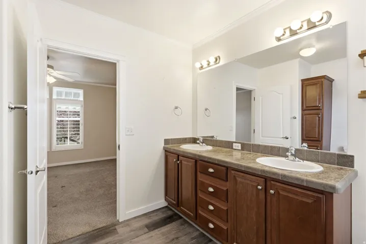 Full bath featuring ornamental molding, double vanity, dark wood finished floors, ceiling fan, and dark carpet