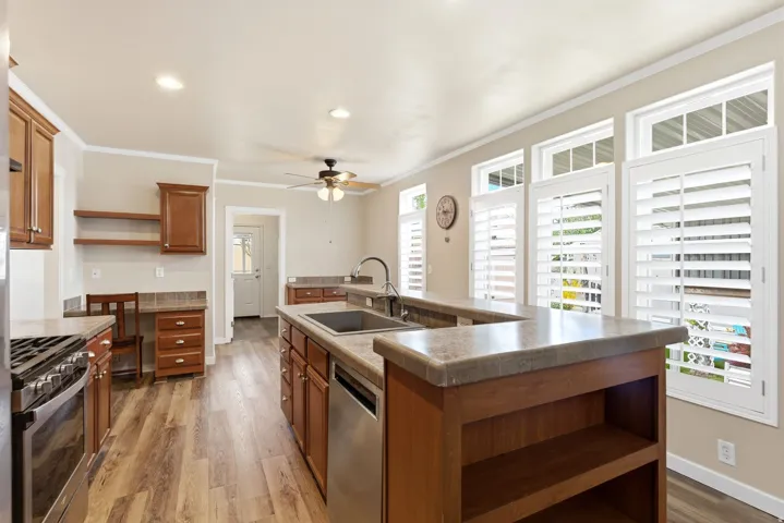 Kitchen with open shelves, a kitchen island with sink, stainless steel appliances, light wood-style flooring, and ceiling fan