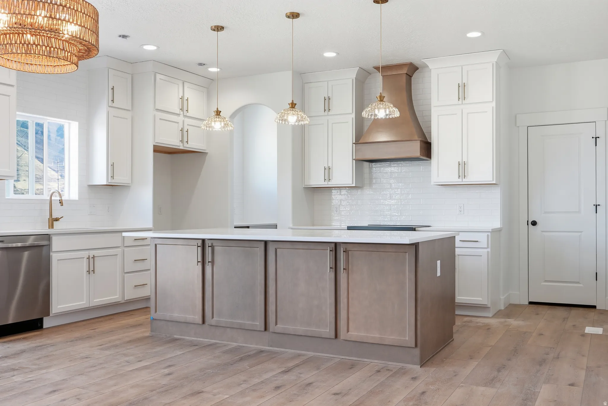 Kitchen with two tone cabinetry, stainless steel dishwasher, light wood finished floors, a center island, and light stone counters
