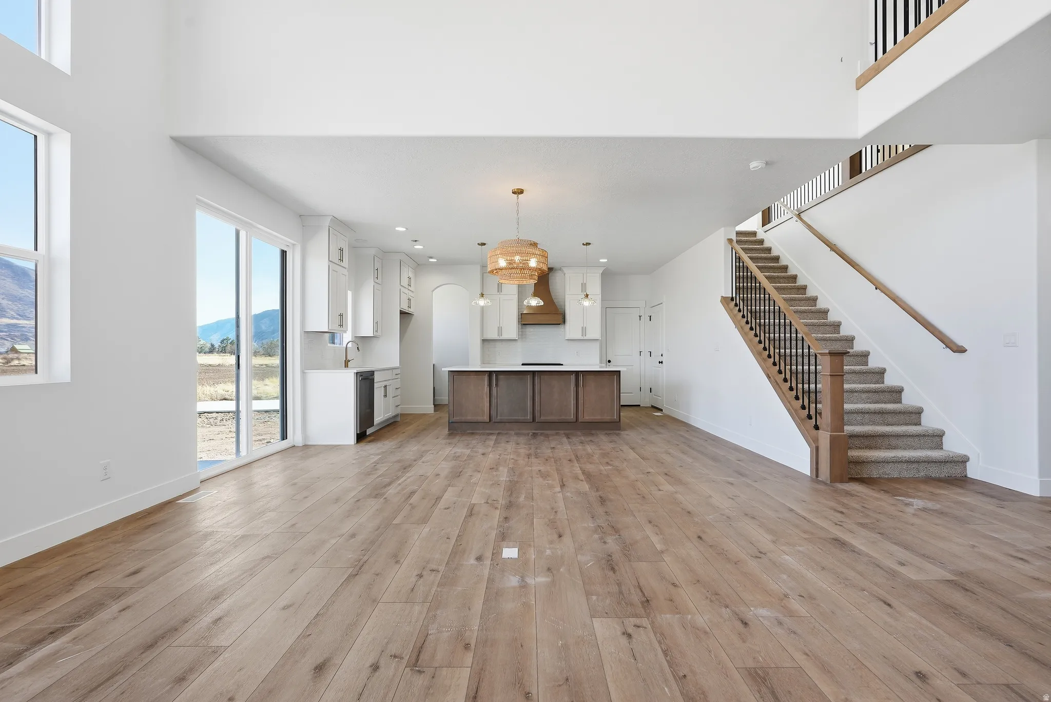 Unfurnished living room with light wood finished floors, hanging lights, a mountain view, and a high ceiling