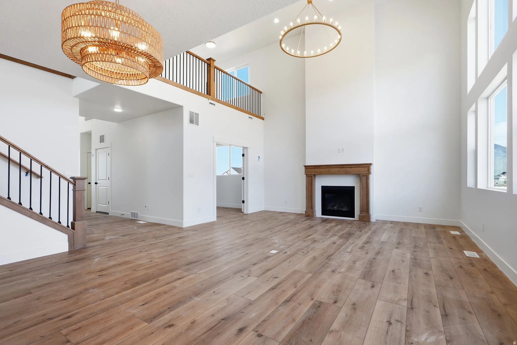 Unfurnished living room featuring suspended lighting, a fireplace, light wood-type flooring, and a high ceiling