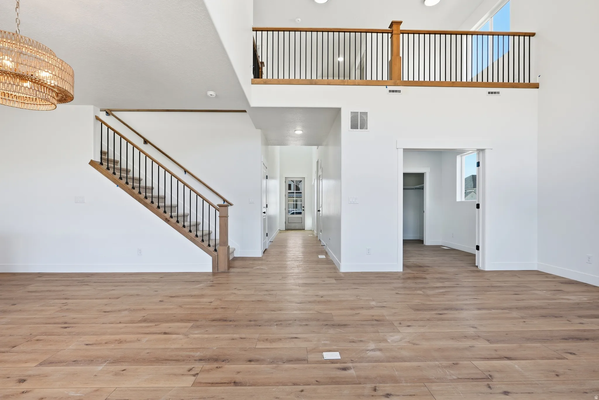 Unfurnished living room featuring light wood finished floors, hanging lights, and a high ceiling