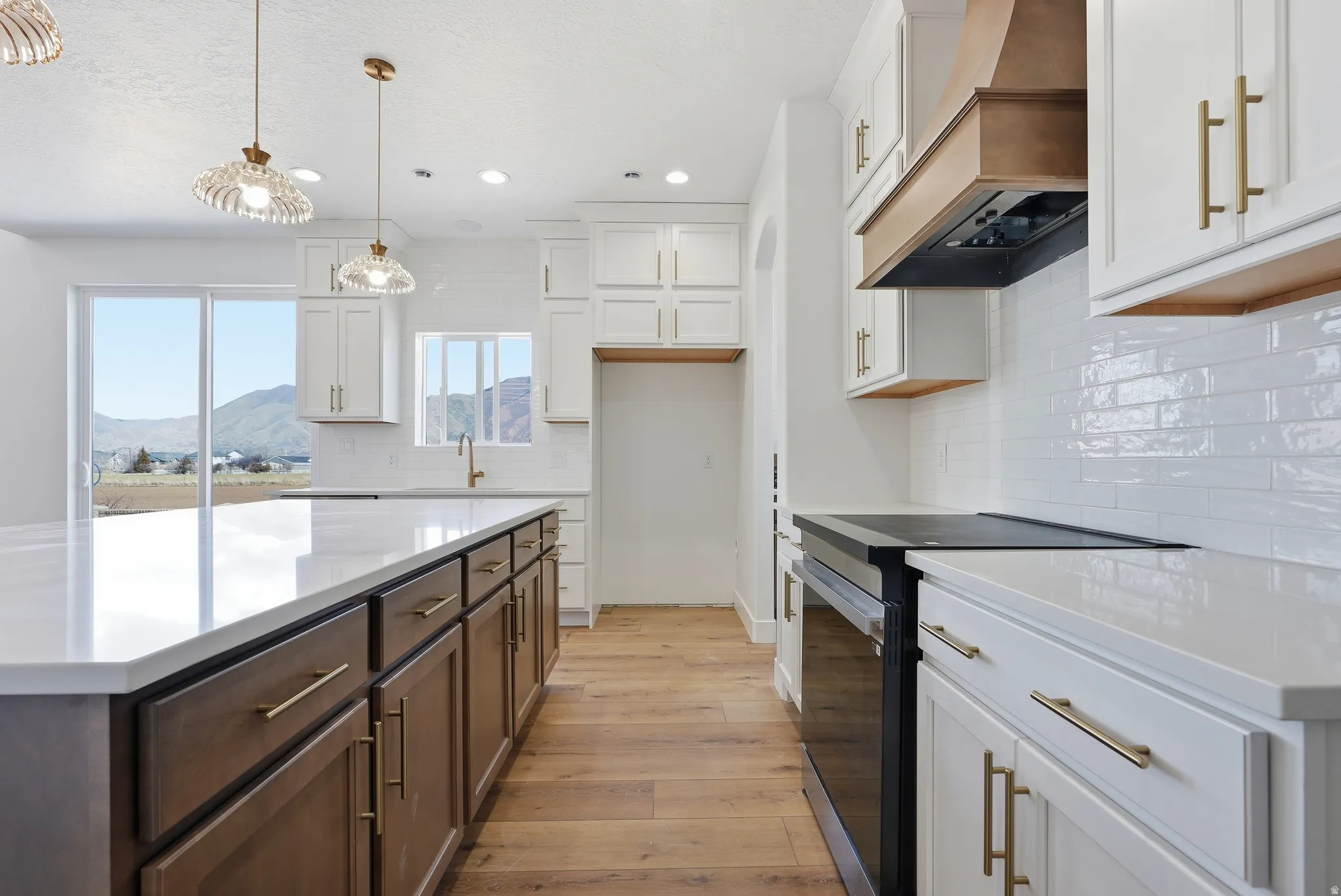 Dual tone kitchen with two tone cabinetry, black range with electric stovetop, light wood-style floors, light stone countertops, and decorative light fixtures