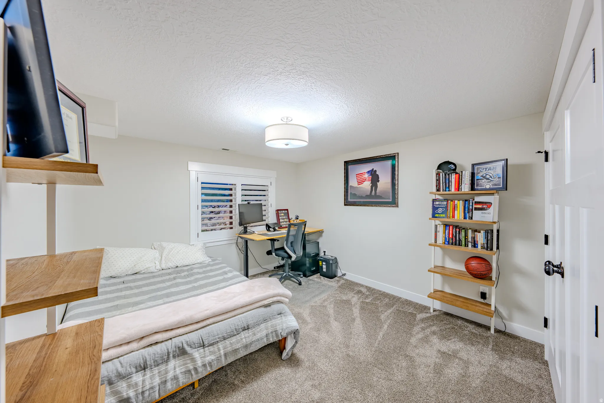 Bedroom with a textured ceiling, light colored carpet, and a desk