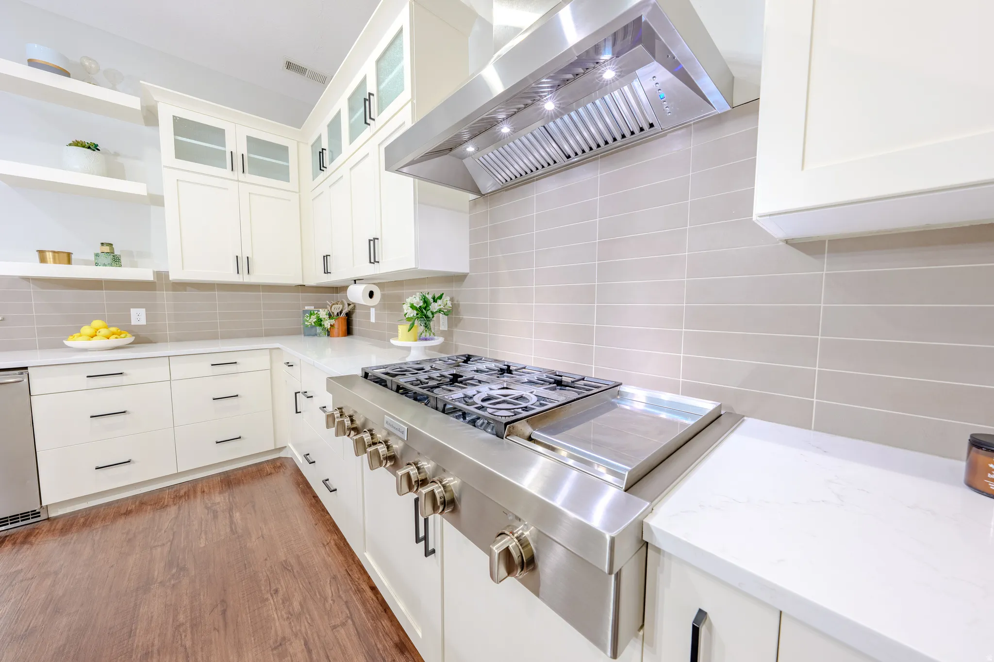 Kitchen with glass insert cabinets, stainless steel gas stovetop, white cabinetry, and backsplash
