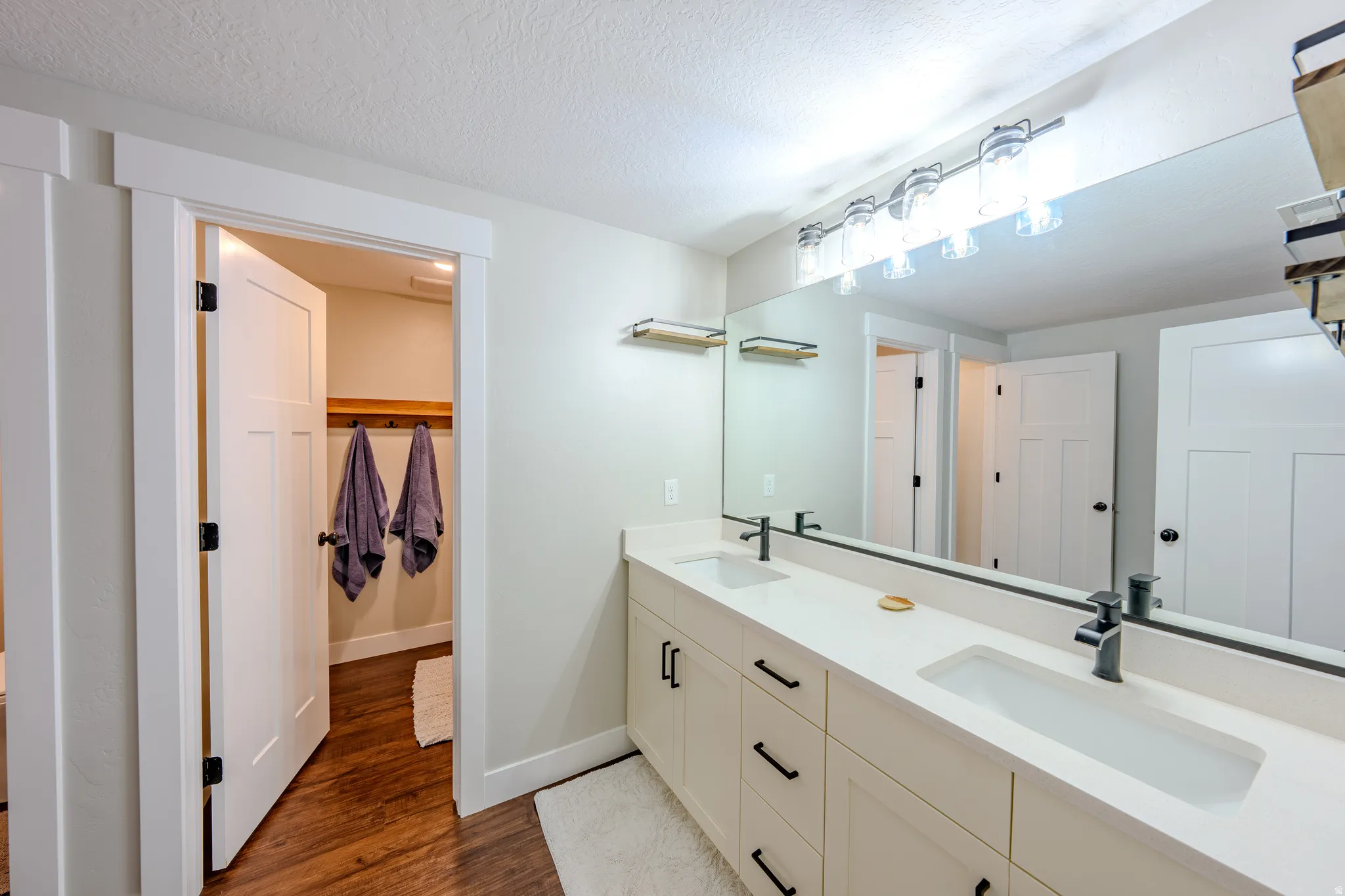 Bathroom featuring double vanity, dark wood-type flooring, and a textured ceiling