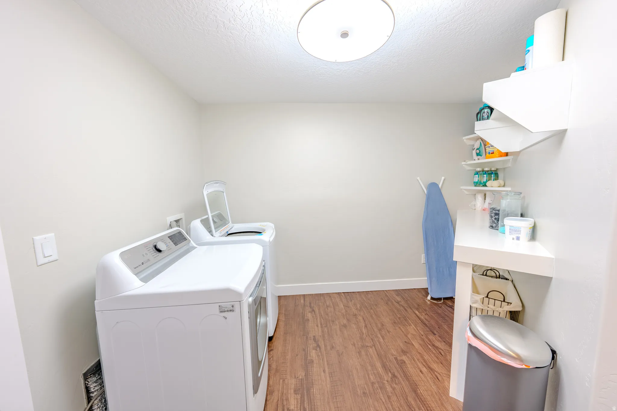 Laundry room with light wood-style flooring, independent washer and dryer, and a textured ceiling