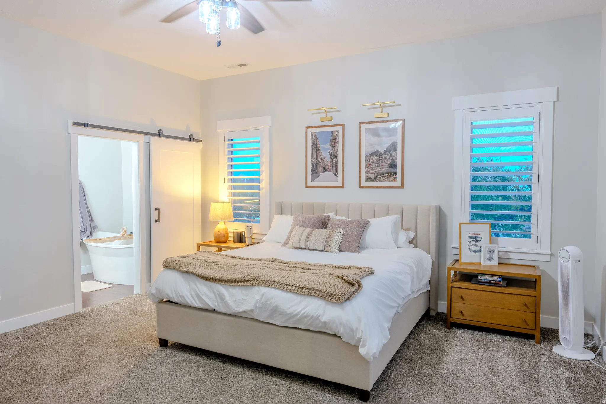 Carpeted bedroom featuring a barn door, ceiling fan, connected bathroom, and multiple windows