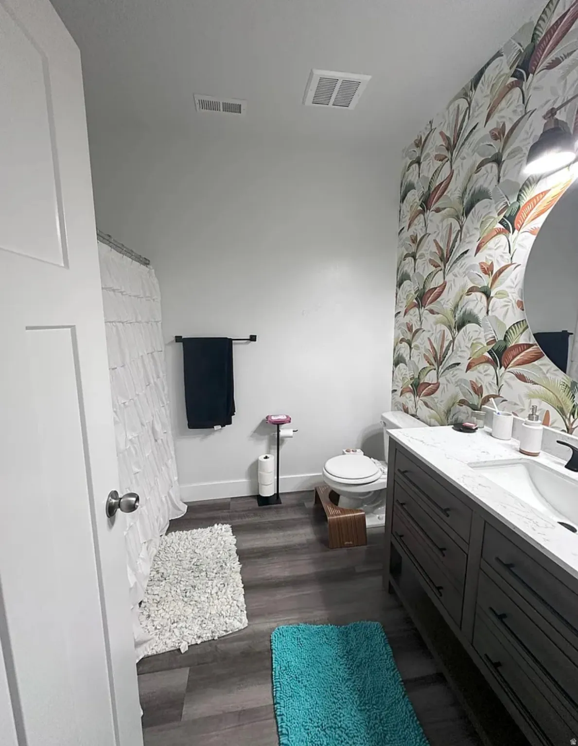 Bathroom with vanity, dark wood finished floors, a shower with curtain, an accent wall, and wallpapered walls