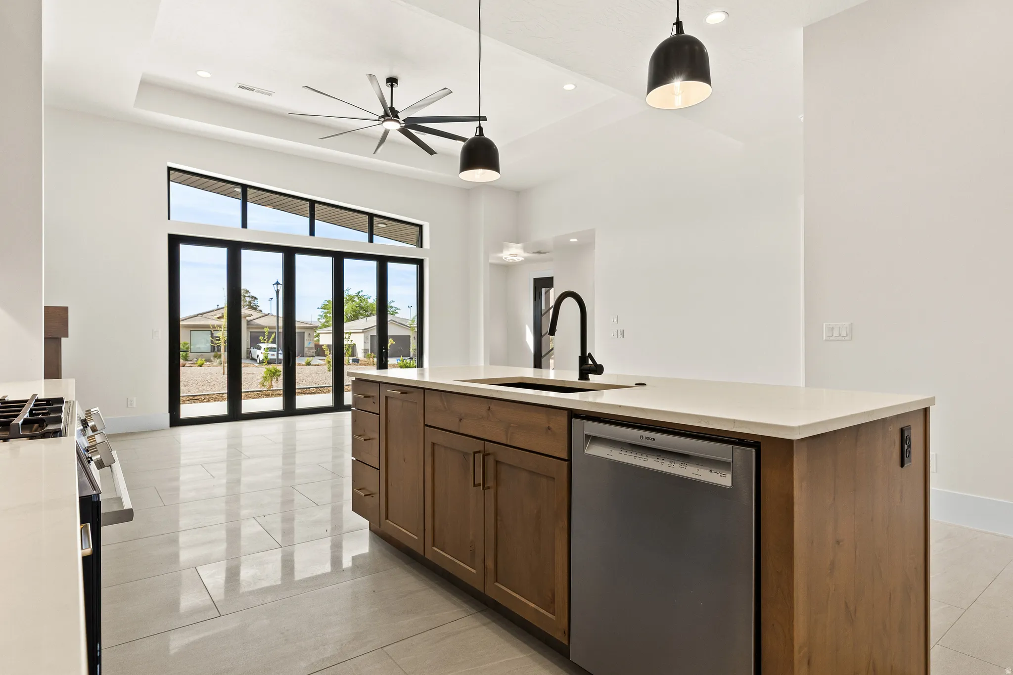 Kitchen with stainless steel appliances, decorative light fixtures, a kitchen island with sink, wood finish cabinetry, and light stone counters