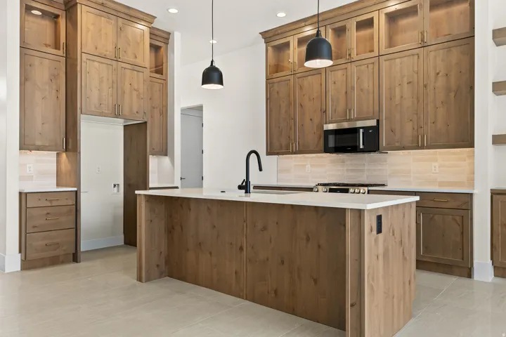 Kitchen featuring tasteful backsplash, a kitchen island with sink, hanging light fixtures, light stone counters, and wood finish cabinetry