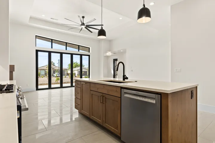 Kitchen with stainless steel appliances, decorative light fixtures, a kitchen island with sink, wood finish cabinetry, and light stone counters