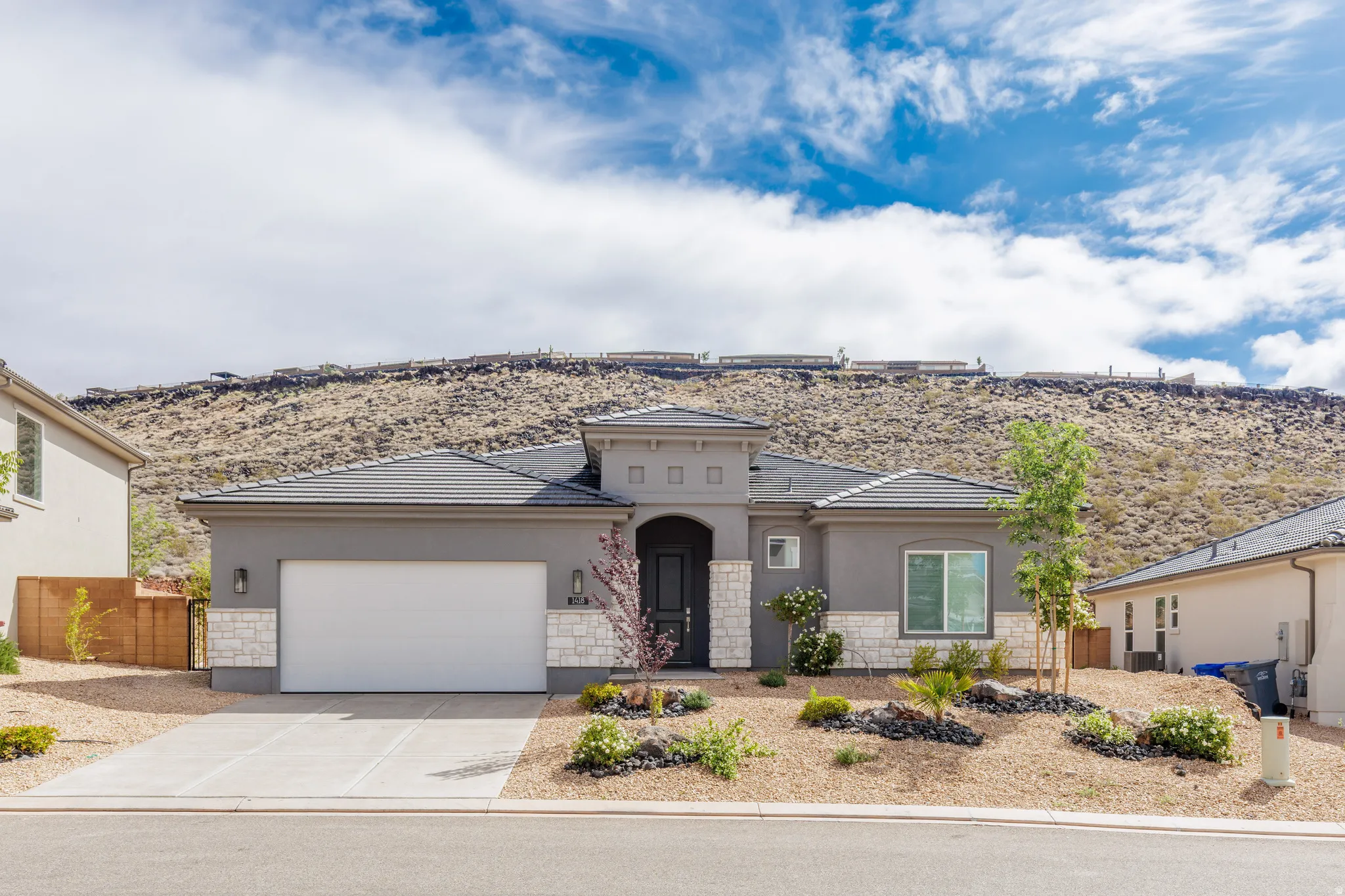 View of front of home featuring stone siding, an attached garage, concrete driveway, stucco siding, and a tiled roof