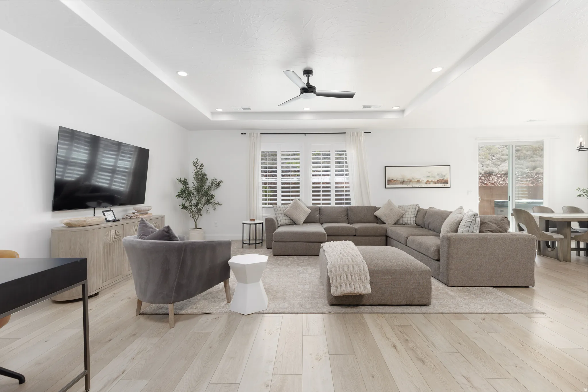 Living area with ceiling fan, light wood-type flooring, healthy amount of natural light, a tray ceiling, and recessed lighting