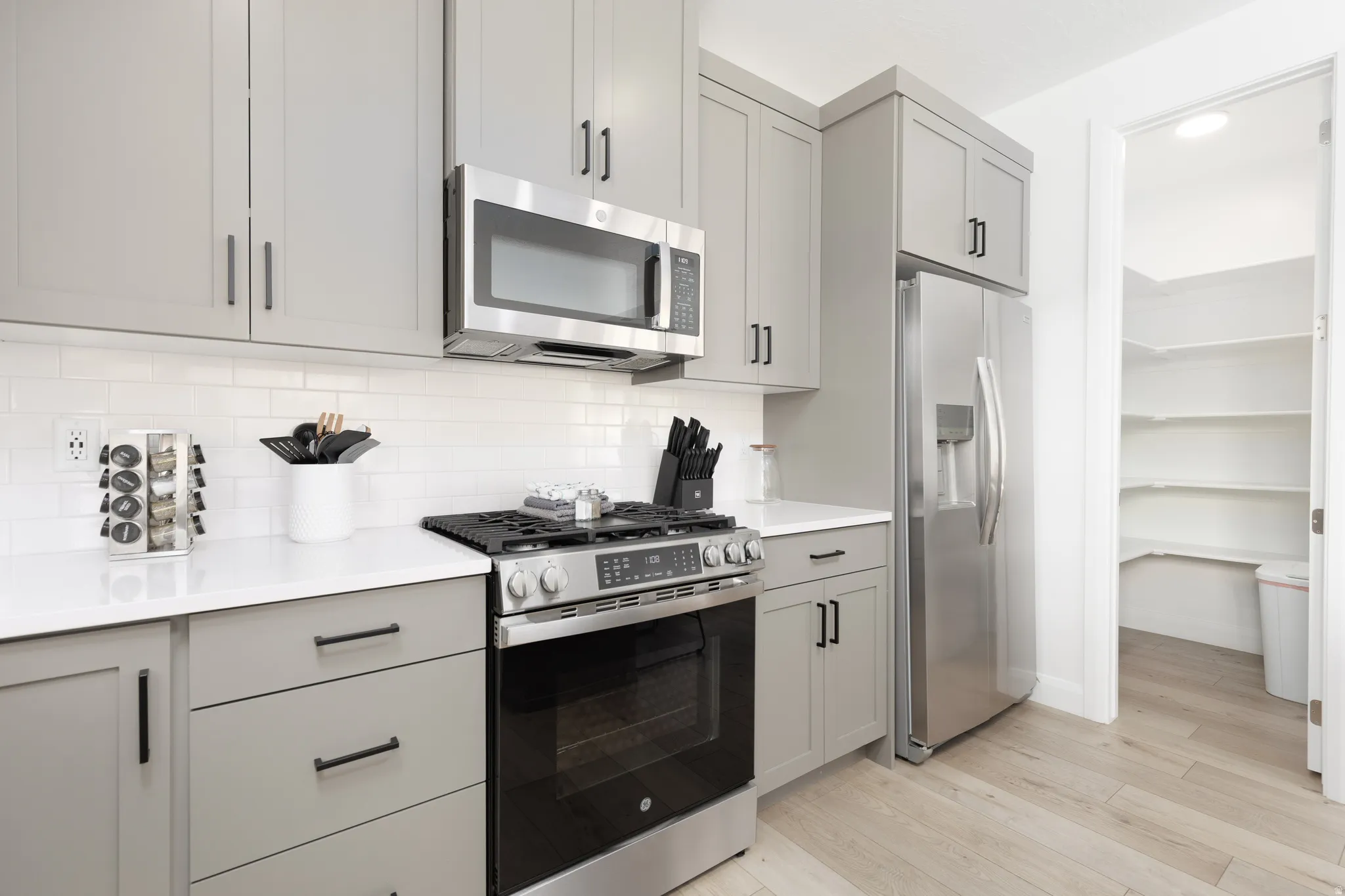 Kitchen featuring gray cabinets, stainless steel appliances, light wood-style floors, decorative backsplash, and light stone counters