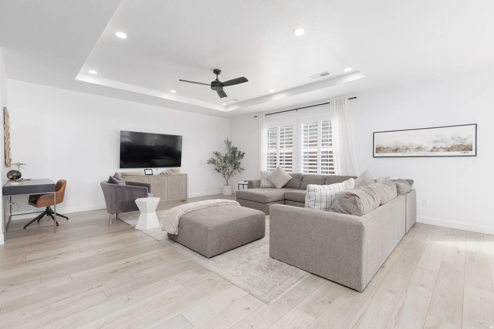 Living area with a desk, light wood-style floors, a ceiling fan, a raised ceiling, and recessed lighting
