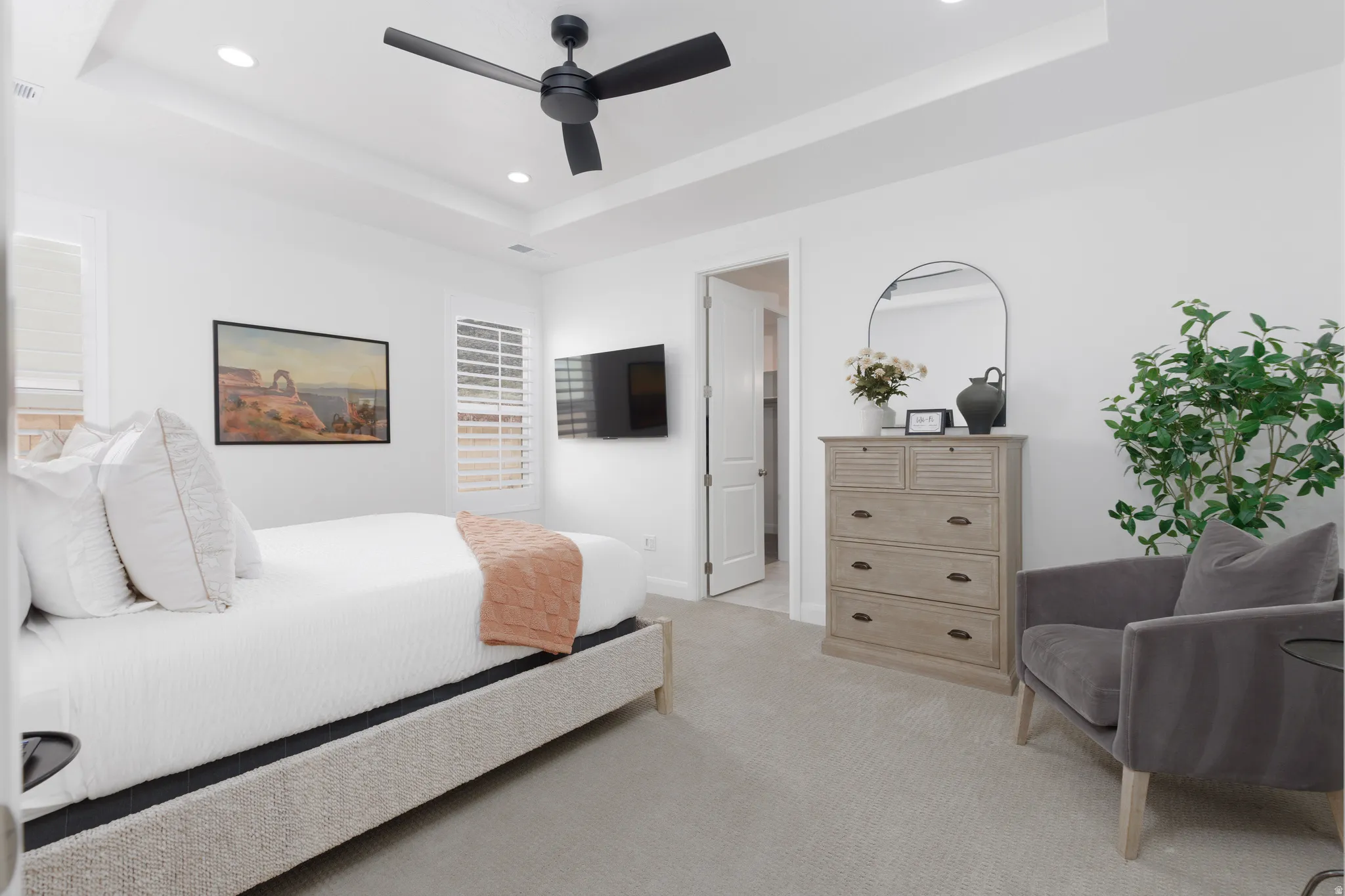 Bedroom with a raised ceiling, recessed lighting, light carpet, ensuite bathroom, and ceiling fan