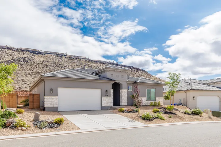View of front of home with stone siding, a gate, an attached garage, stucco siding, and concrete driveway