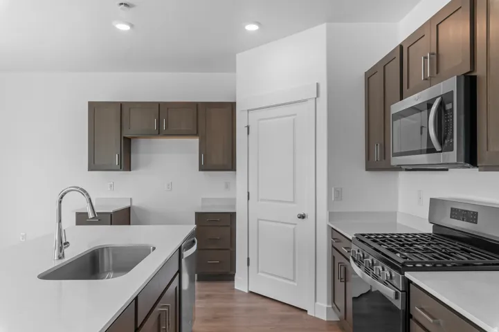 Kitchen featuring dark wood-finish cabinetry, light countertops, a stainless steel gas range, and a stainless steel microwave