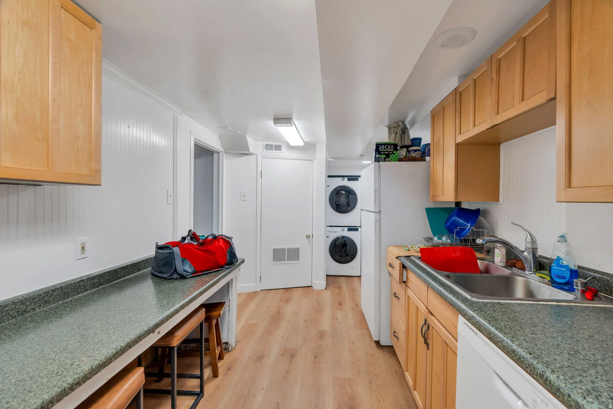 Kitchen with dark countertops, white appliances, light wood-style floors, and light wood finish cabinetry