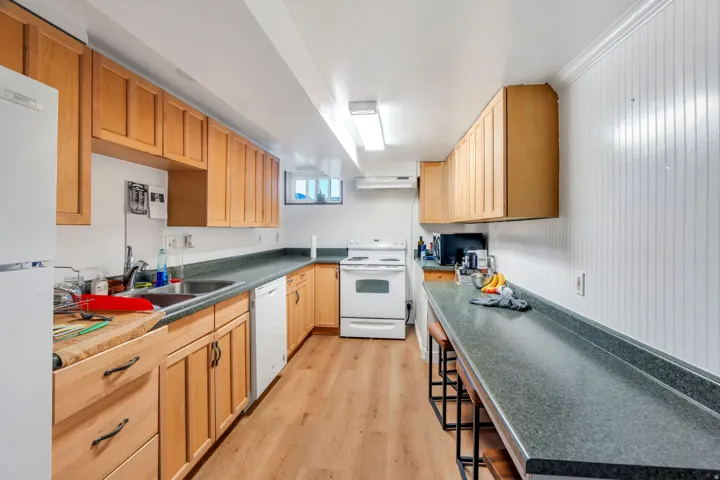 Kitchen featuring dark countertops, white appliances, light wood-style flooring, light wood finish cabinetry, and a breakfast bar
