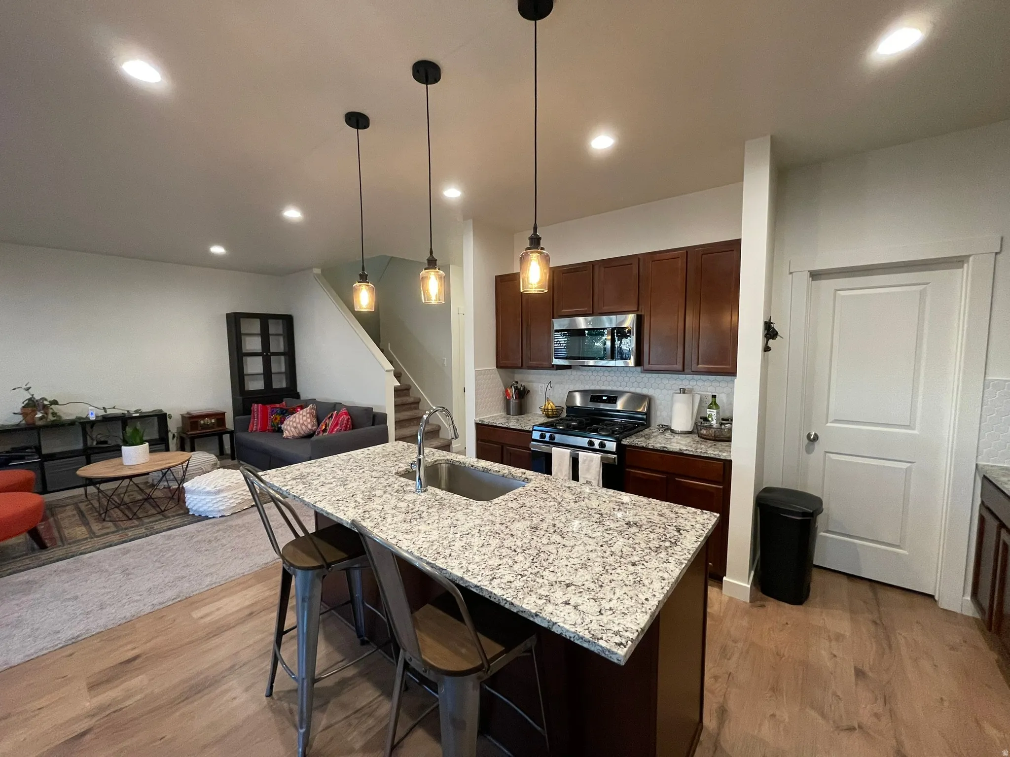 Kitchen featuring a breakfast bar, light stone counters, light wood-style floors, stainless steel appliances, and open floor plan