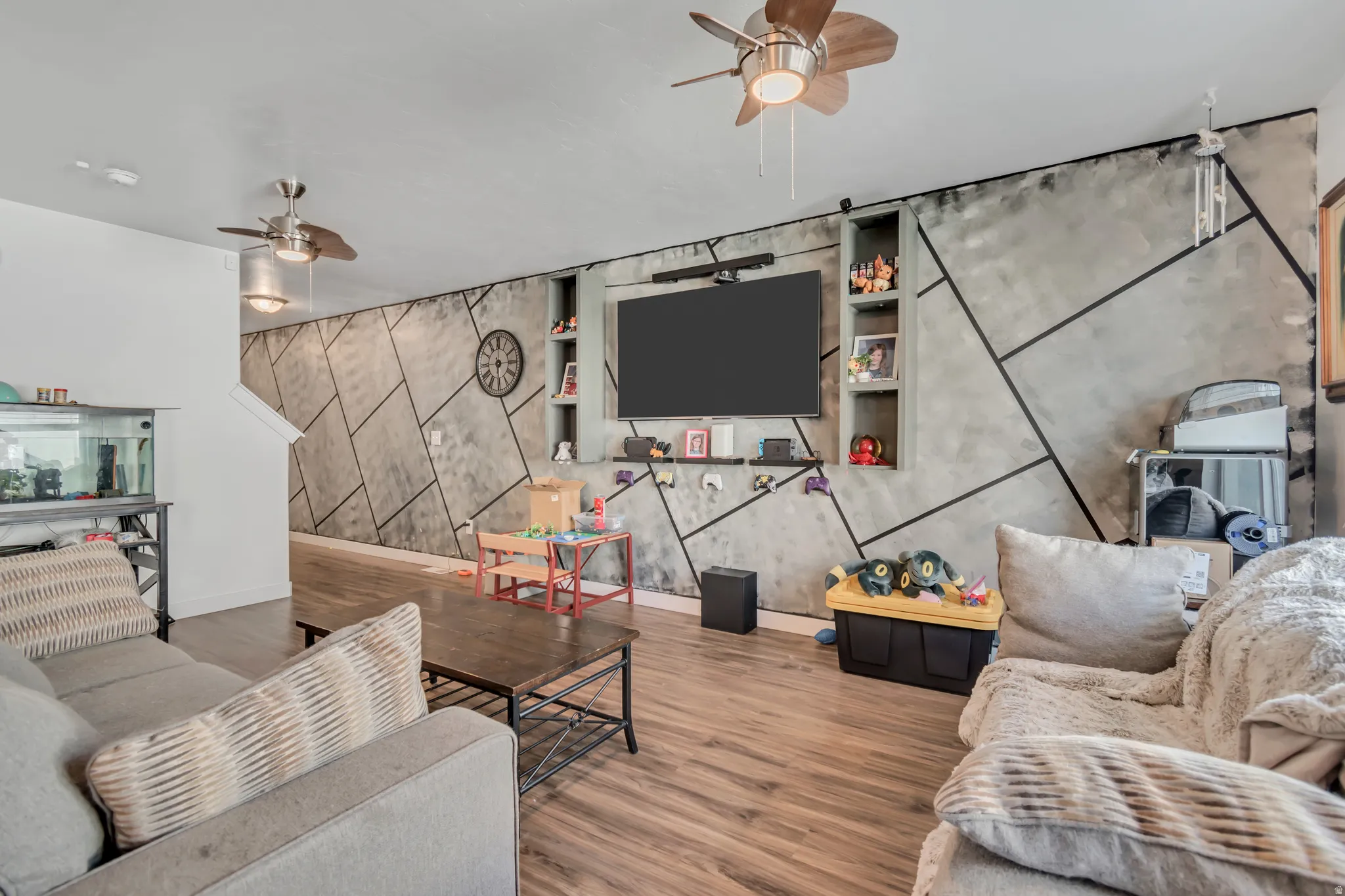 Living room with an accent wall, ceiling fan, and wood finished floors