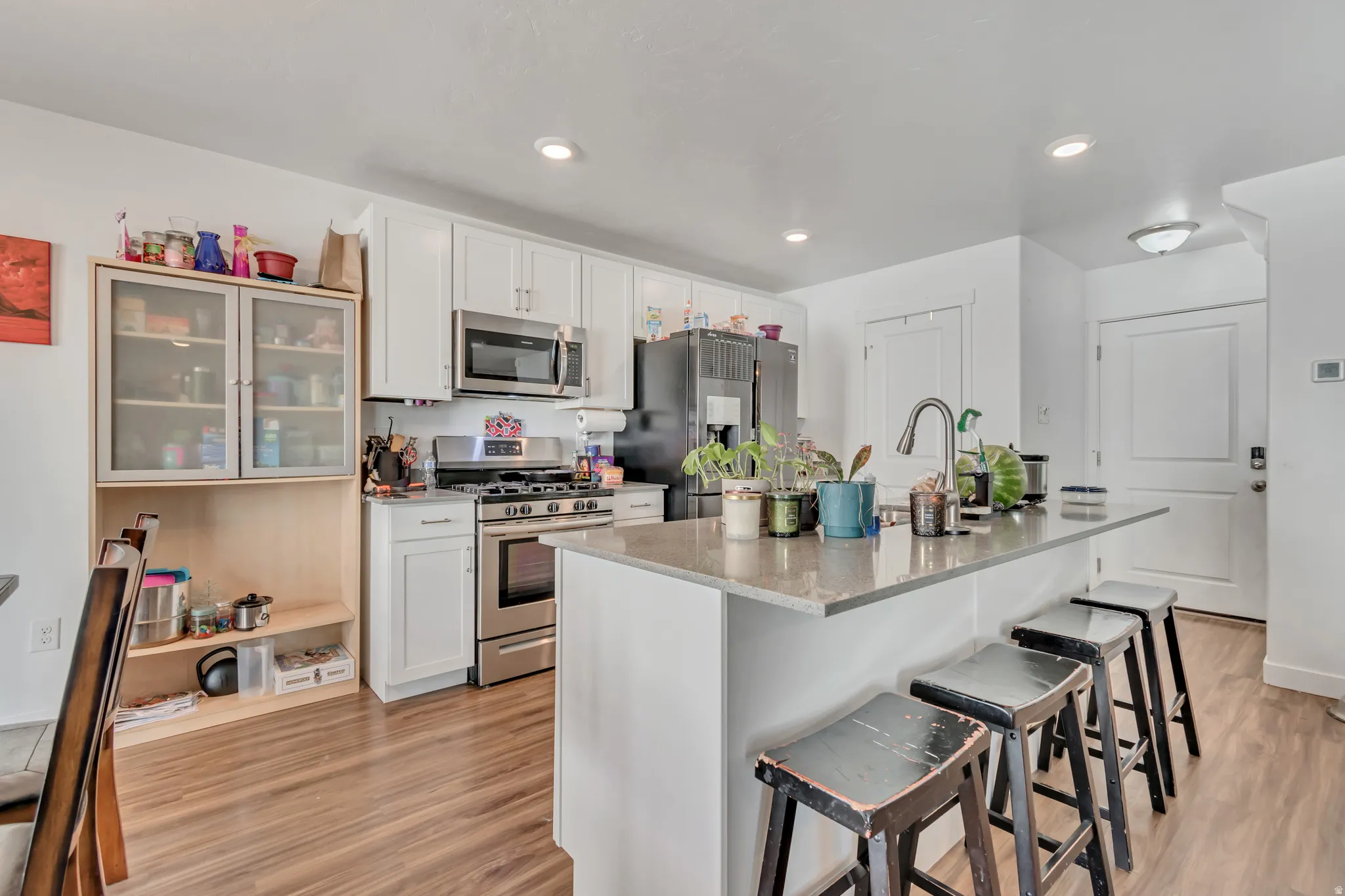 Kitchen featuring stainless steel appliances, a kitchen bar, light wood-type flooring, white cabinetry, and recessed lighting