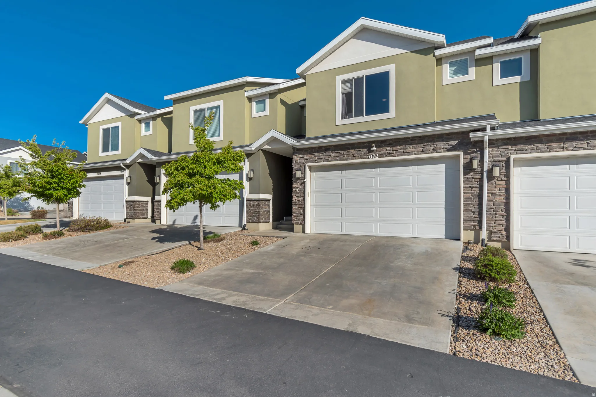 View of front of property featuring stucco siding, an attached garage, stone siding, and driveway