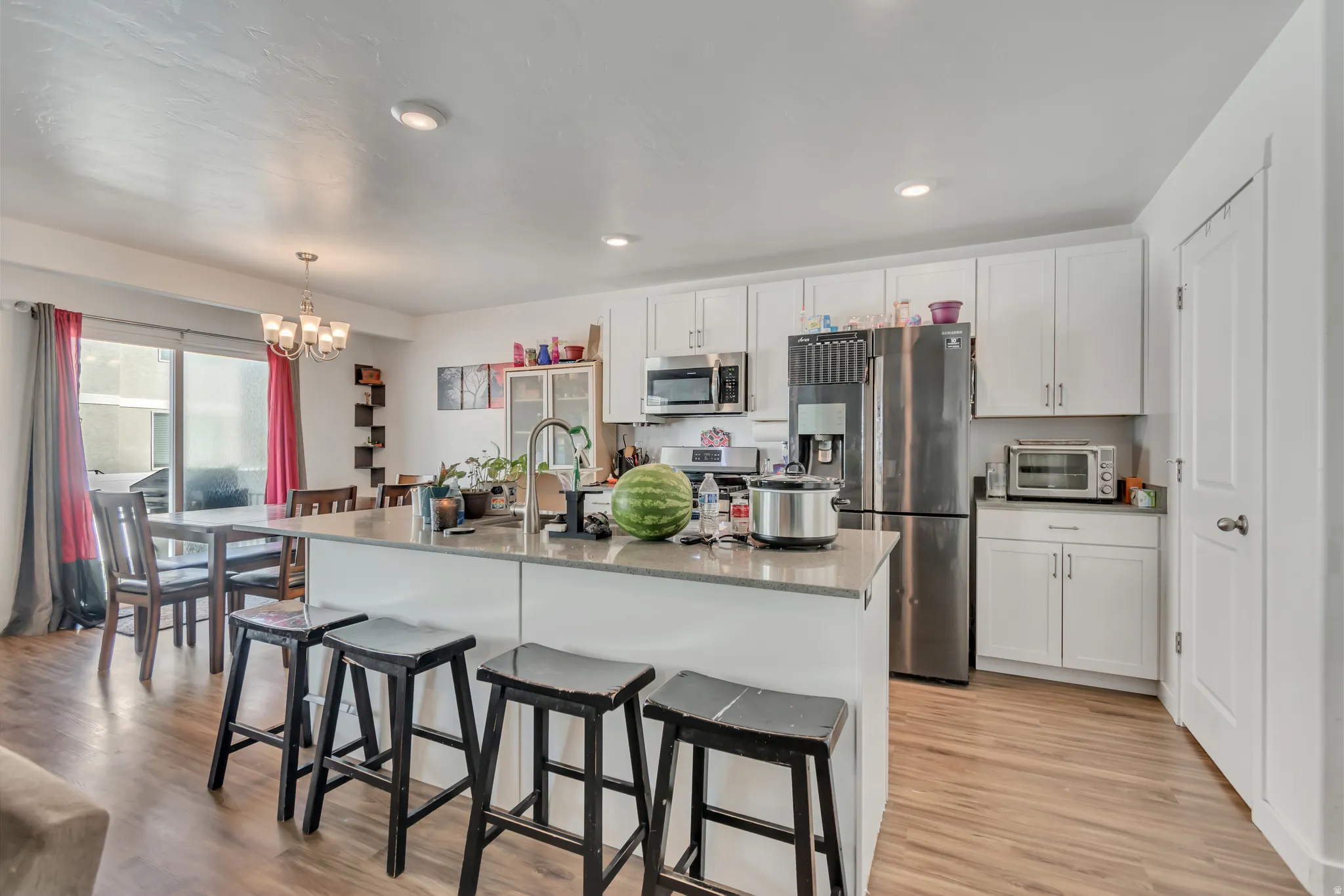 Kitchen with stainless steel appliances, light wood-type flooring, white cabinetry, a chandelier, and a kitchen bar