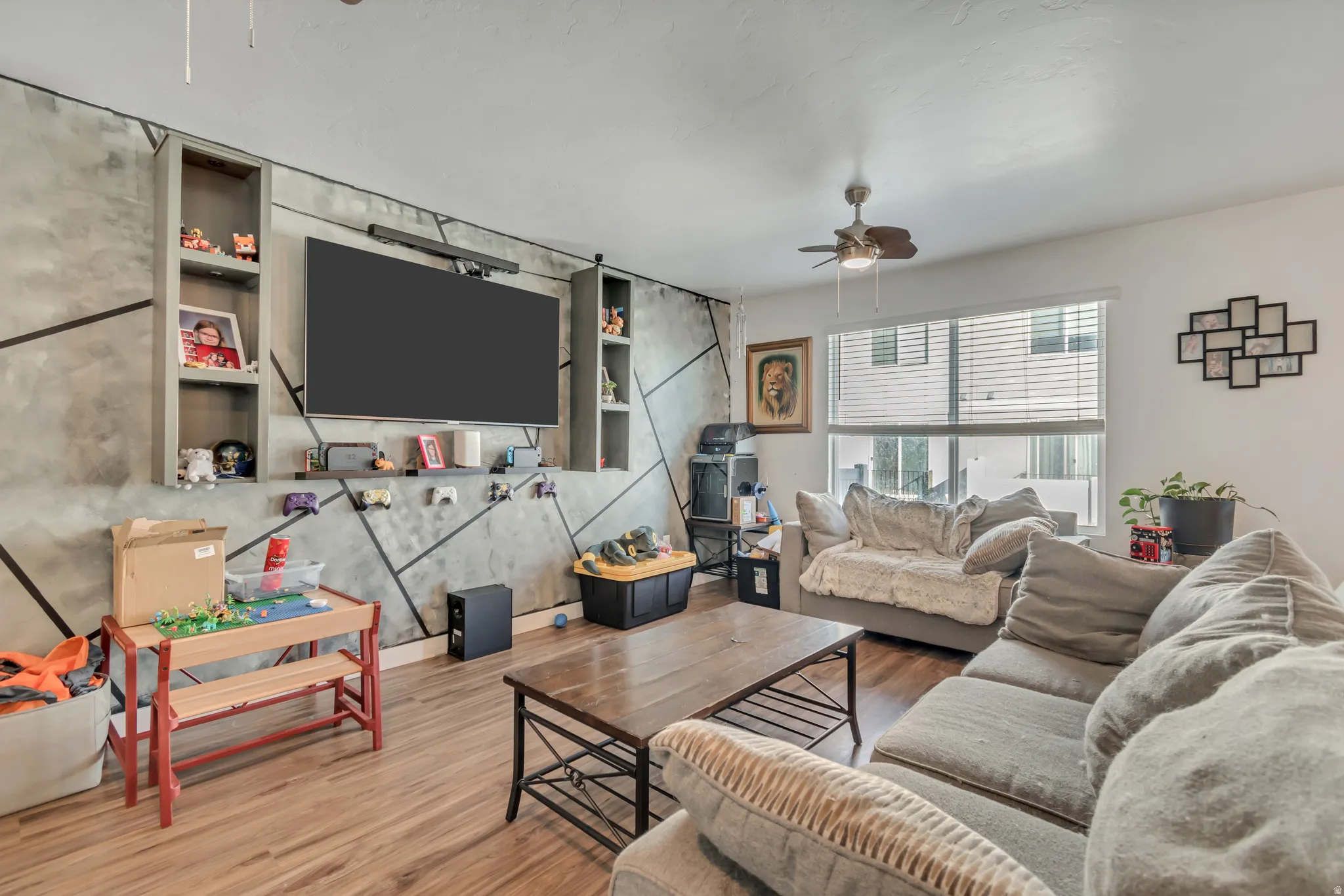Living area with wood finished floors, a ceiling fan, and an accent wall