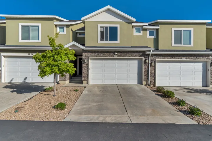 View of front of house featuring stucco siding, an attached garage, driveway, and stone siding