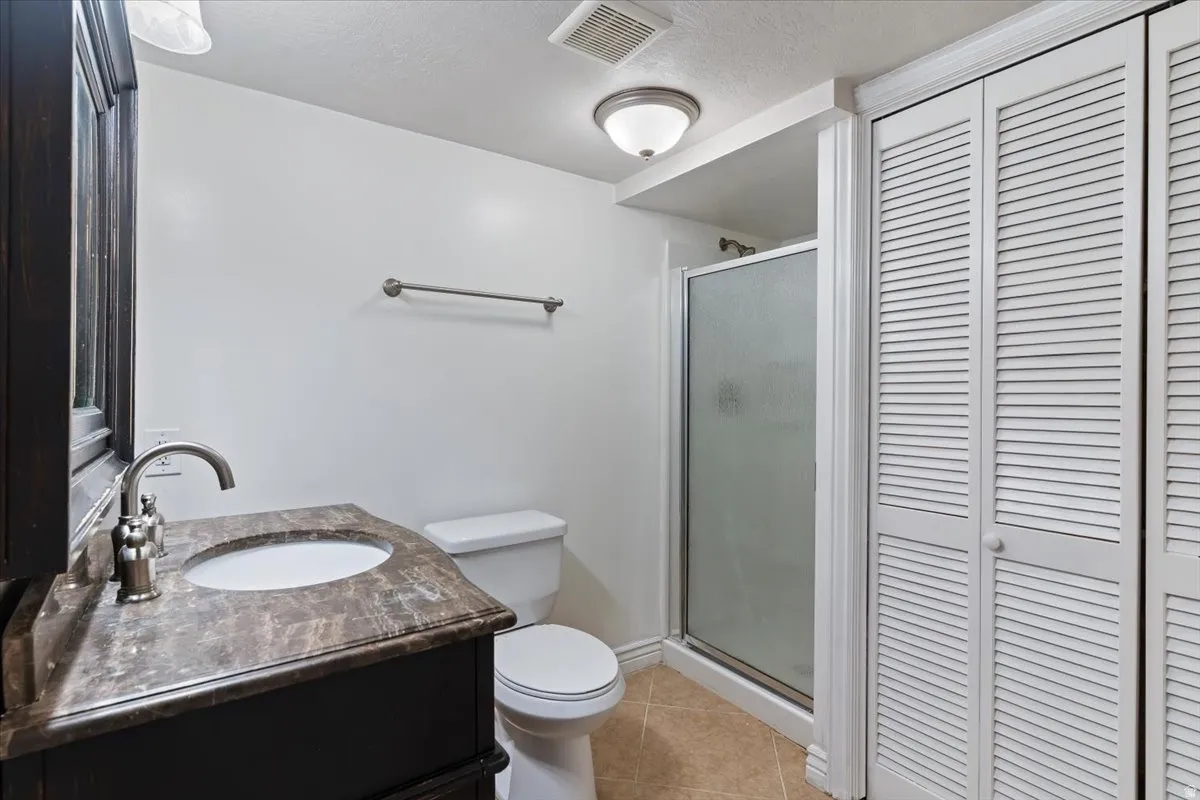 Full bathroom featuring vanity, light tile patterned floors, a closet, a stall shower, and a textured ceiling