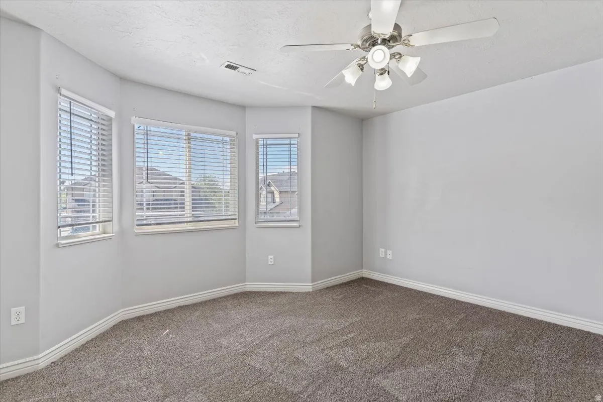 Empty room with a ceiling fan and dark carpet