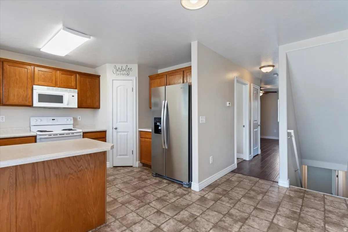 Kitchen featuring white appliances, light countertops, stone finish floors, and wood finish cabinets