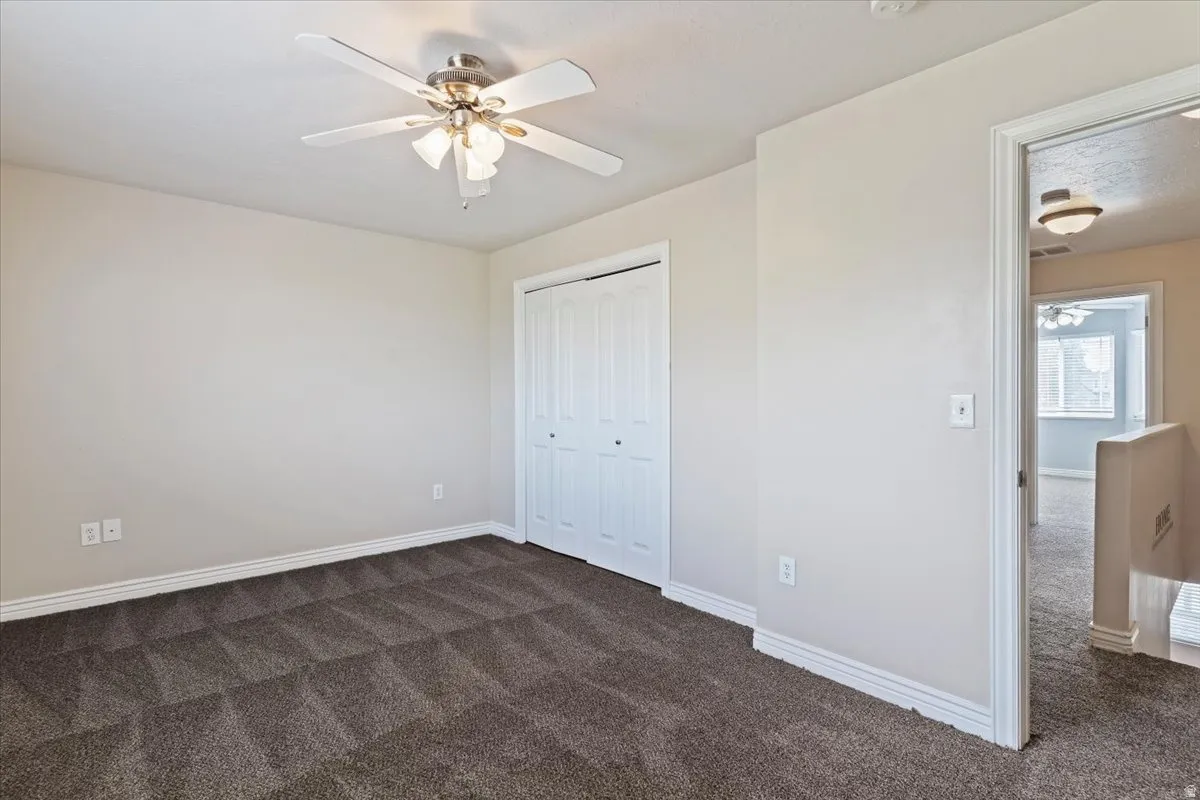 Unfurnished bedroom with dark colored carpet, a closet, and a ceiling fan