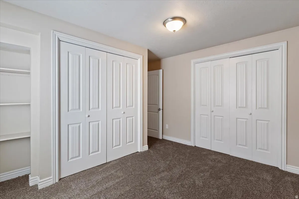 Unfurnished bedroom featuring dark colored carpet and multiple closets