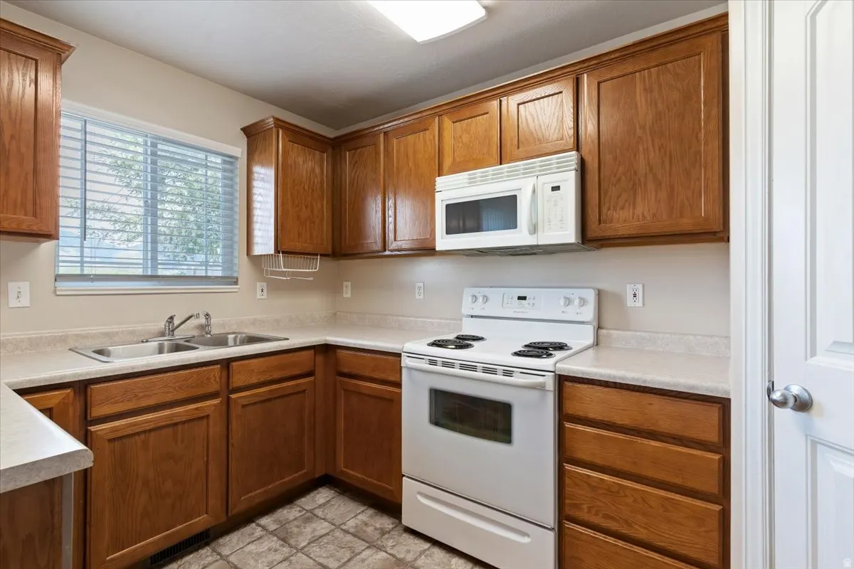 Kitchen with white appliances, wood finish cabinetry, and light countertops
