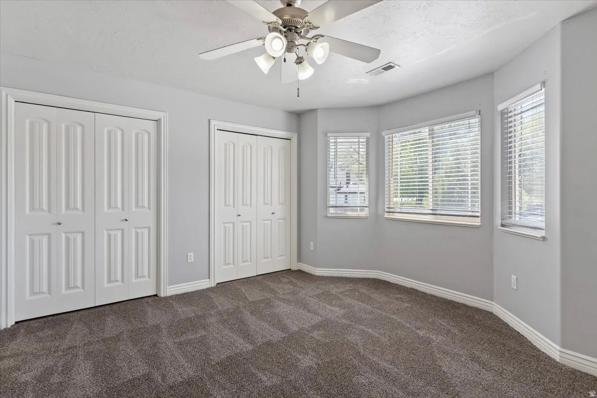 Unfurnished bedroom with multiple closets, dark colored carpet, a textured ceiling, and a ceiling fan