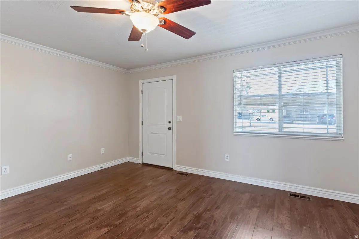 Empty room featuring a ceiling fan, dark wood-style flooring, and crown molding