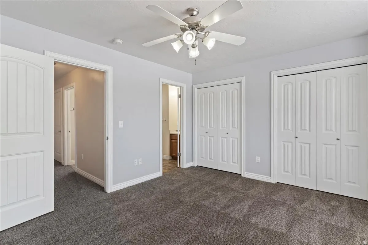 Unfurnished bedroom featuring multiple closets, dark colored carpet, a ceiling fan, and ensuite bathroom