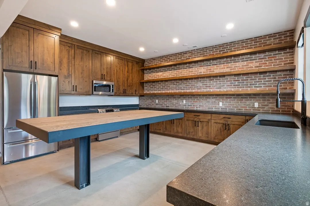 Kitchen with stainless steel appliances, open shelves, brick wall, recessed lighting, and finished concrete floors