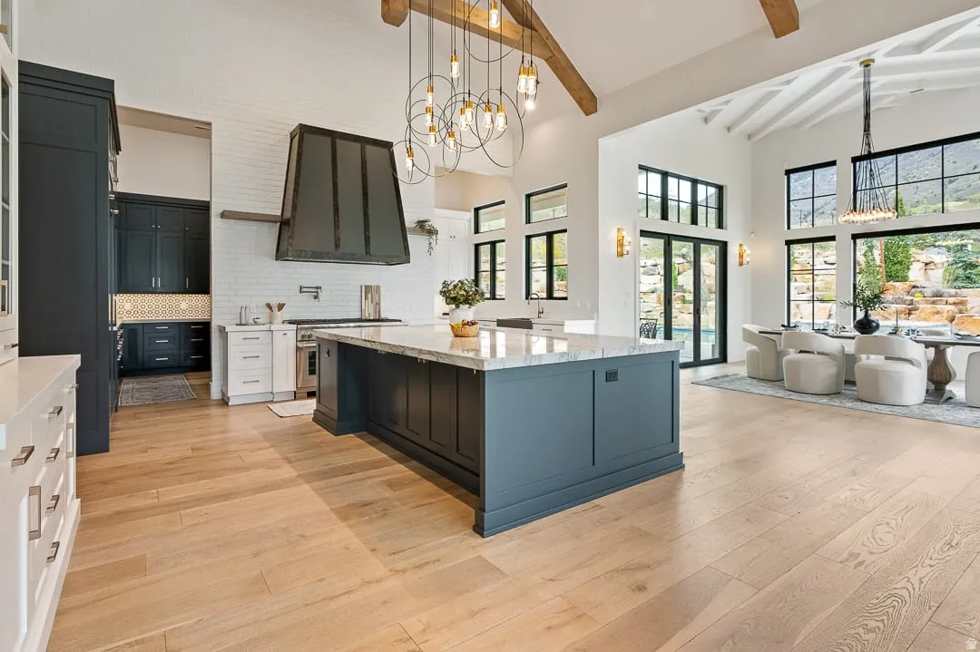 Two tone kitchen with a chandelier, light stone countertops, a spacious island, light wood-style floors, and dual tone cabinetry