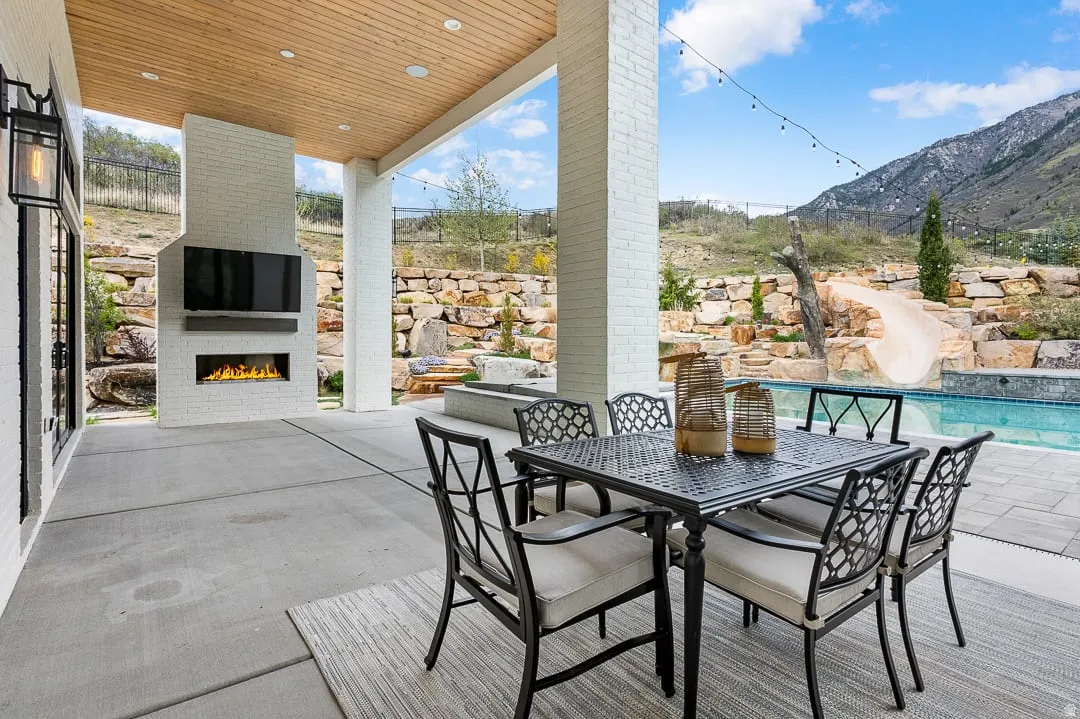 View of patio with a lit fireplace, outdoor dining space, and an outdoor pool