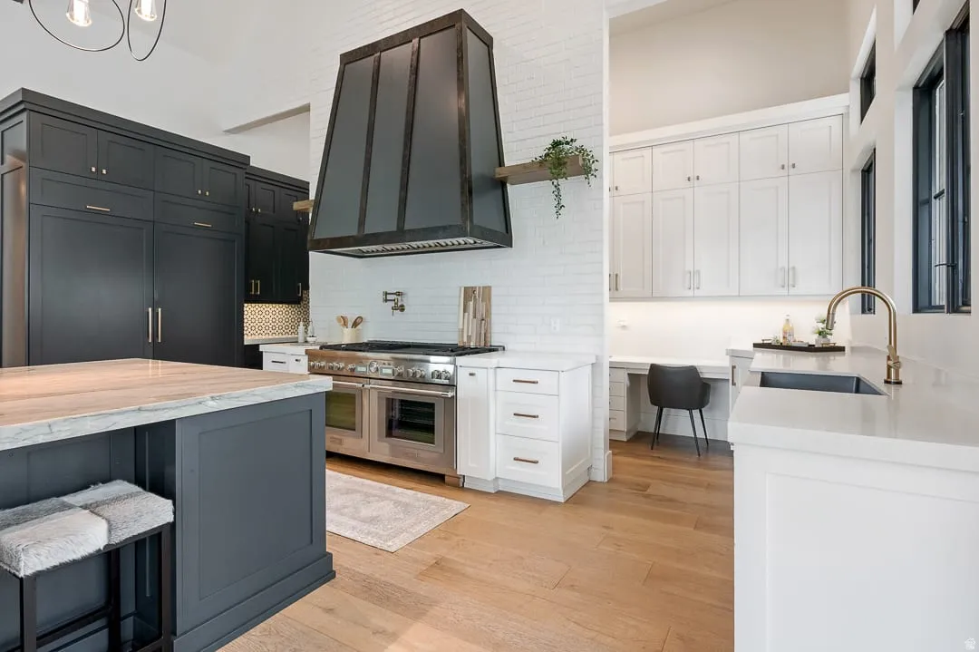Kitchen with light stone countertops, light wood-style flooring, double oven range, a high ceiling, and tasteful backsplash