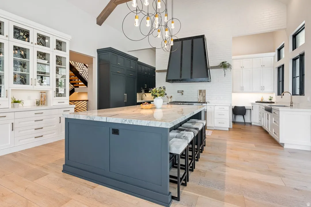 Kitchen with light stone counters, light wood-style floors, a kitchen island, two tone cabinets, and a chandelier