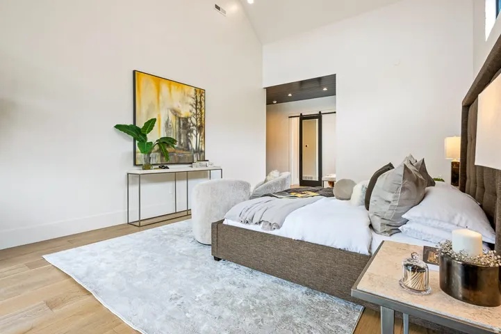 Bedroom featuring a barn door, light wood-style floors, recessed lighting, and lofted ceiling